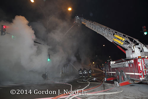firemen use E-ONE tower ladder to battle commercial fire at night