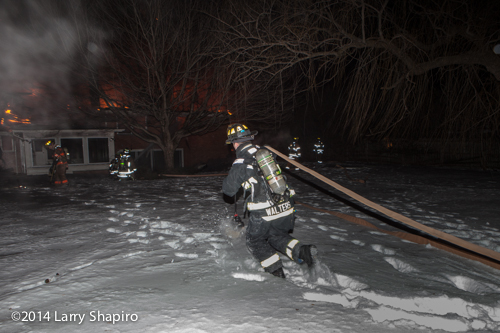 fireman pulls hose through snow at night house fire