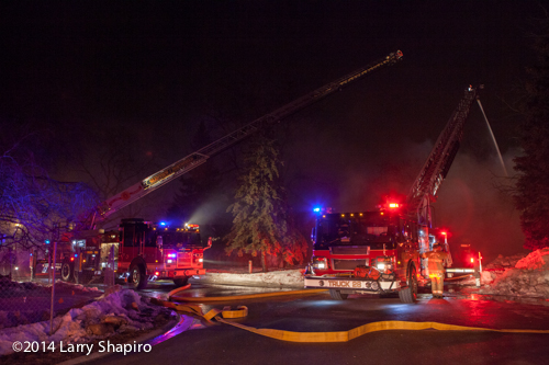 two aerial ladder trucks at night fire scene with master streams