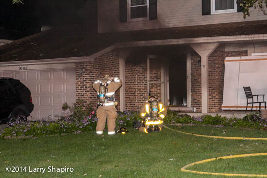 smoke pushes from a house at night as firefighters prepare to enter