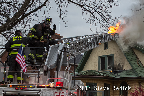 firemen on ladder with flames through roof