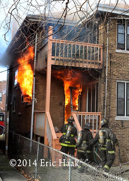 firemen with hose enter house with flames