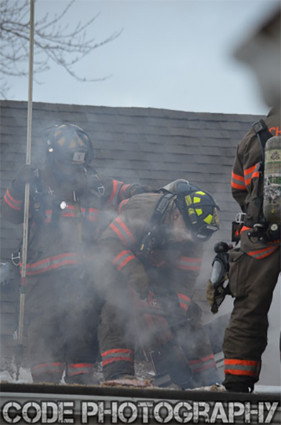 firemen on roof with saws and smoke