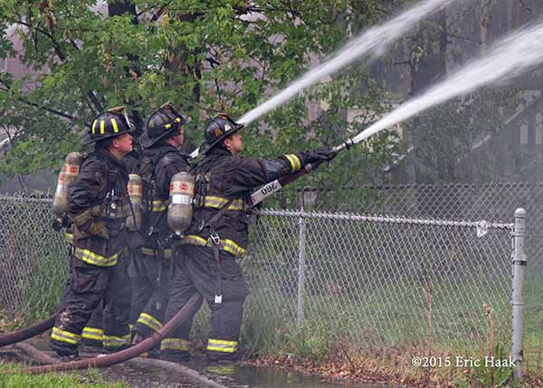 firemen with hose lines on chainlink fence