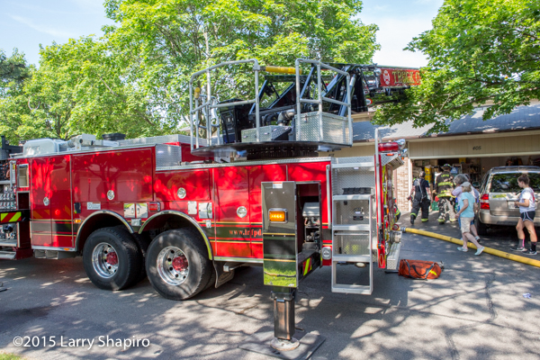 Pierce ladder truck positioned through dense trees at fire scene