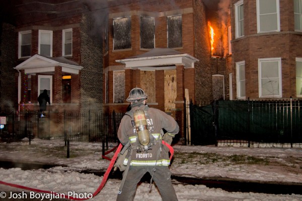 firefighter pulls hose a building burns at night