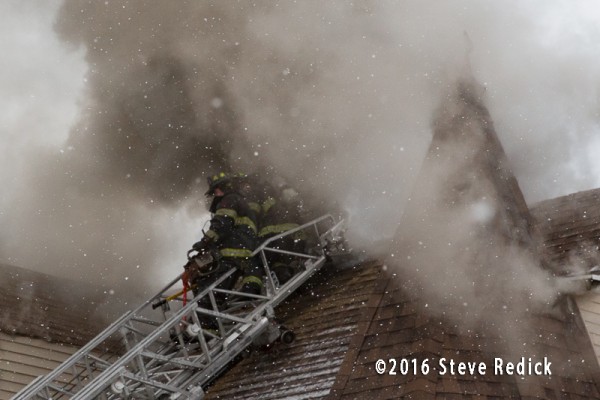 firemen vent roof at fire with heavy smoke