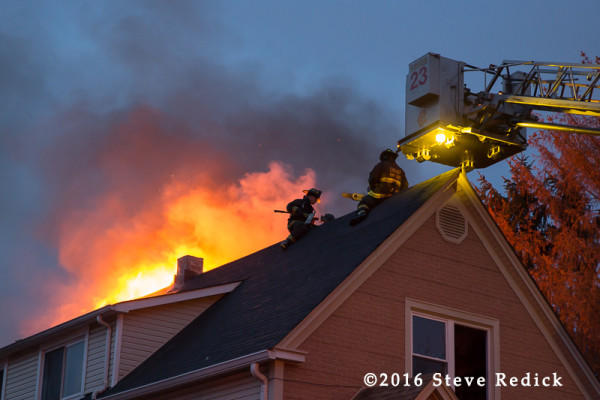 firemen on peak roof with fire at night
