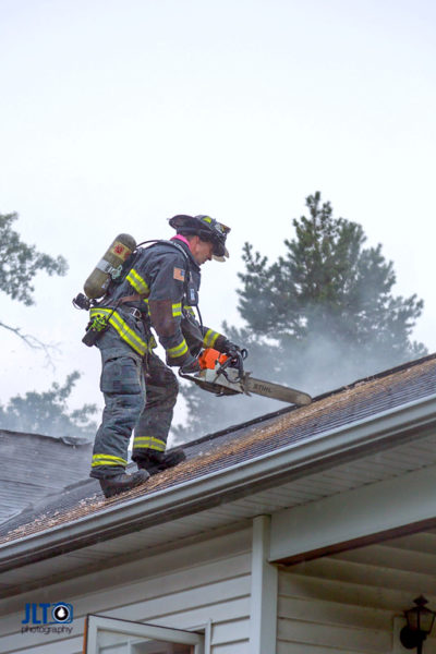 firefighter on roof ventilating house during a fire with a saw