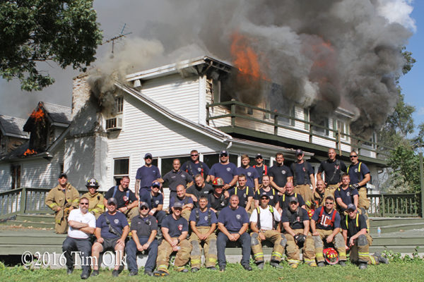 firefighters pose with burning building