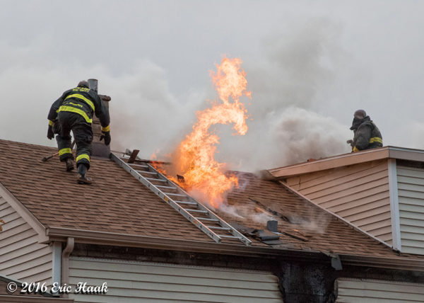 flames through the roof of a house with Firefighters