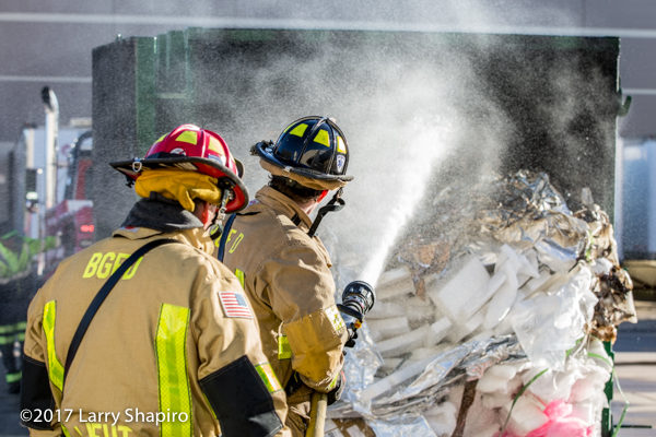 Firefighters with hose dousing dumpster fire