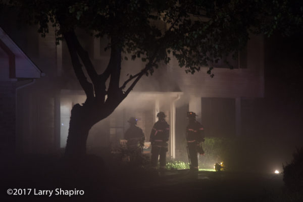 firefighters prepare to enter a house as heavy smoke pushes from basement fire