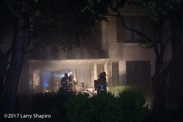 firefighters prepare to enter a house as heavy smoke pushes from basement fire