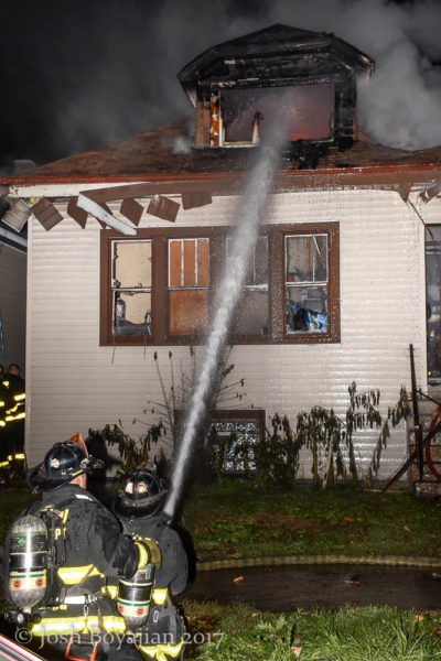 firefighter with hose line battles house fire at night