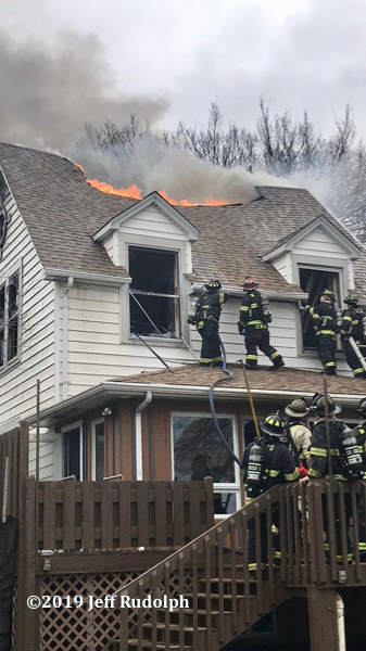 Firefighters battle fire in a large house with flames through the roof